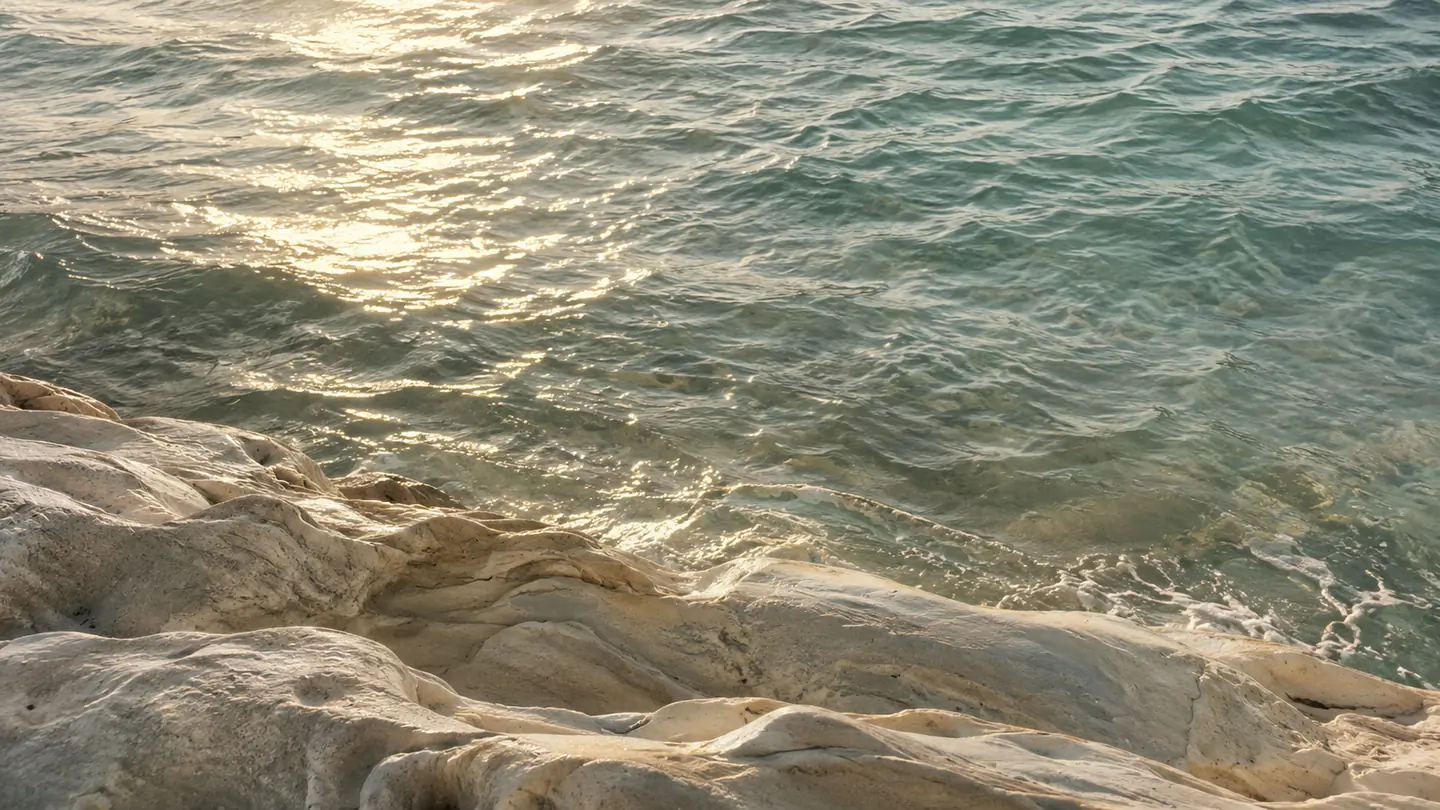 Sunlit sea water washing against pale, weathered shoreline rock.